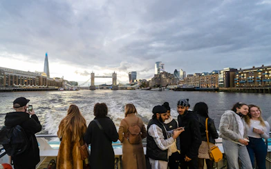 Passengers enjoying Thames River Uber Boat Tour with view of Tower Bridge and London skyline.