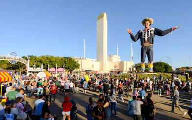 Crowd at State Fair of Texas with Big Tex statue and Cotton Bowl in background.