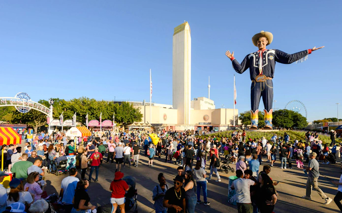 Crowd at State Fair of Texas with Big Tex statue and Cotton Bowl in background.