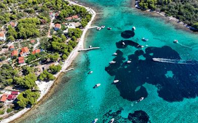 Boats in Blue Lagoon's turquoise waters near Trogir, Croatia, with lush coastline and red-roofed houses.