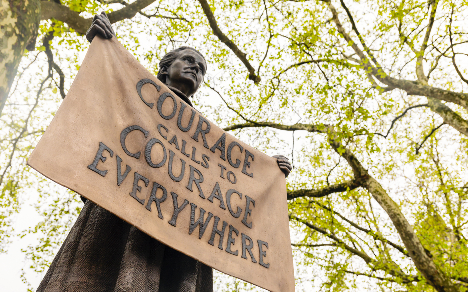Statue holding "Courage Calls to Courage Everywhere" banner near Houses of Parliament, London.