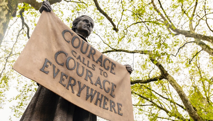 Statue holding "Courage Calls to Courage Everywhere" banner near Houses of Parliament, London.