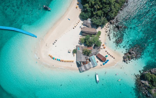 Aerial view of Khai Island beach with colorful umbrellas and speedboat in turquoise water, Phuket tour.