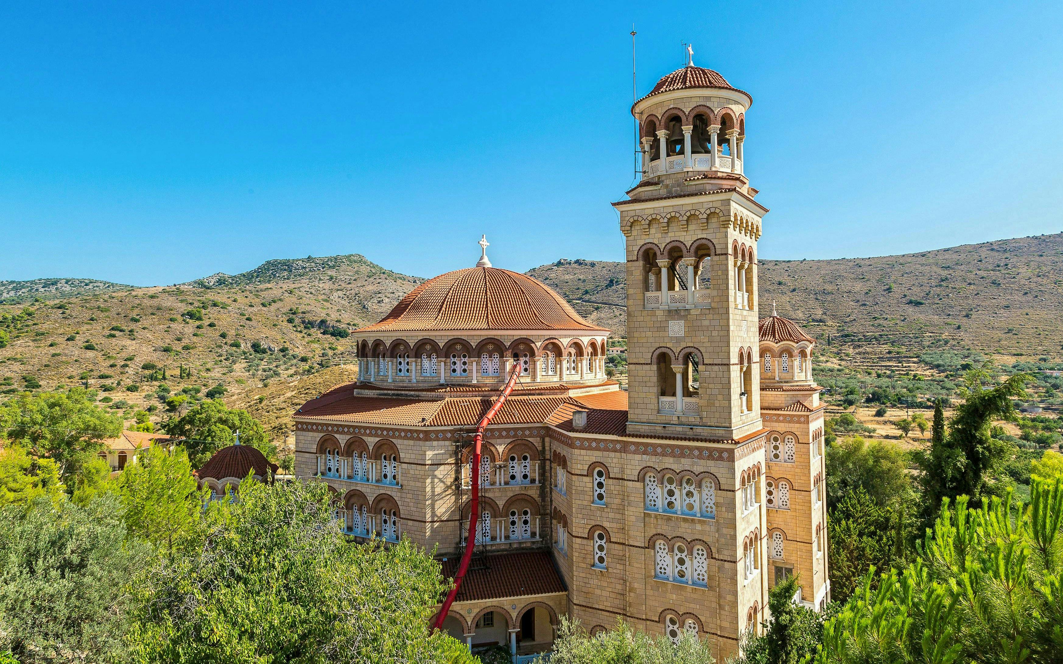 Saint Nektarios church with bell tower on Aegina island, Greece, surrounded by hills.