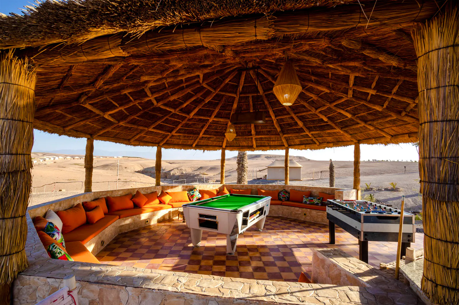 Outdoor lounge with pool table and foosball under a thatched roof in Marrakesh desert setting.