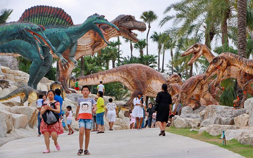 Visitors walking among dinosaur sculptures at Nong Nooch Tropical Garden, Thailand.