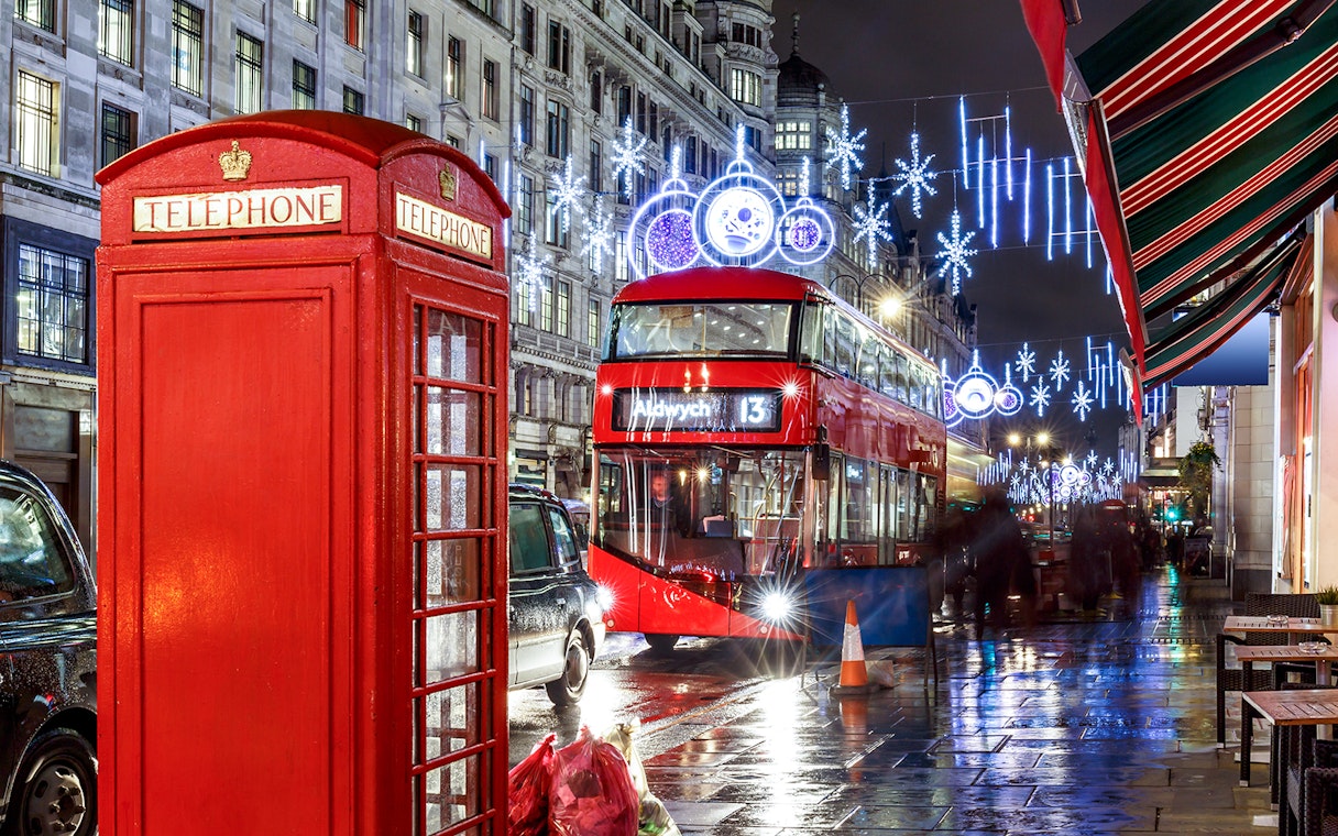 Red double-decker bus and phone booth under Christmas lights in London.