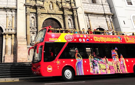Open-top sightseeing bus in Lima, Peru, passing by a historic building.