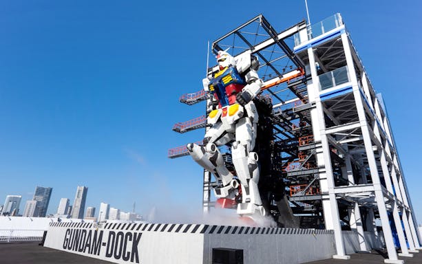 Giant Gundam robot at Gundam Factory Yokohama with city skyline in background.