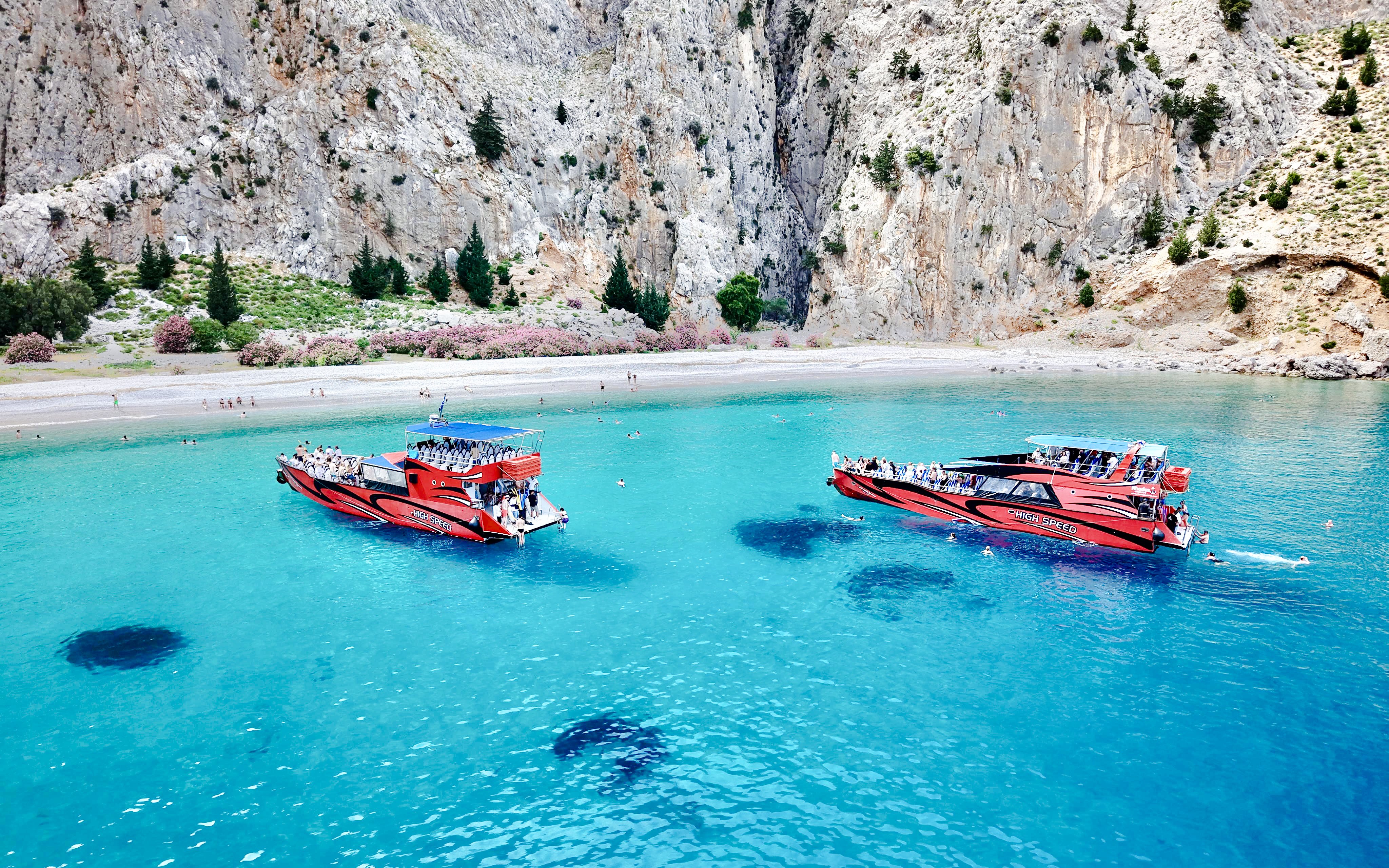 High-speed cruise boats on turquoise waters near rocky cliffs in Rhodes.