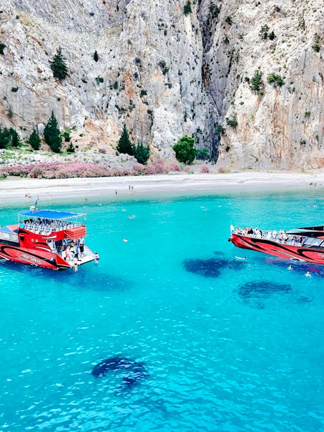 High-speed cruise boats on turquoise waters near rocky cliffs in Rhodes.