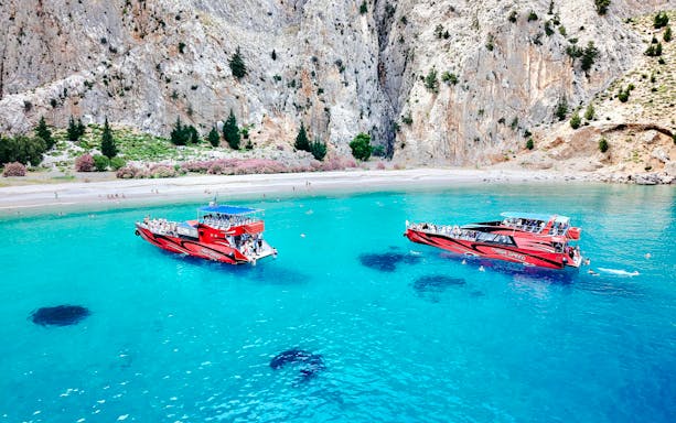 High-speed cruise boats on turquoise waters near rocky cliffs in Rhodes.