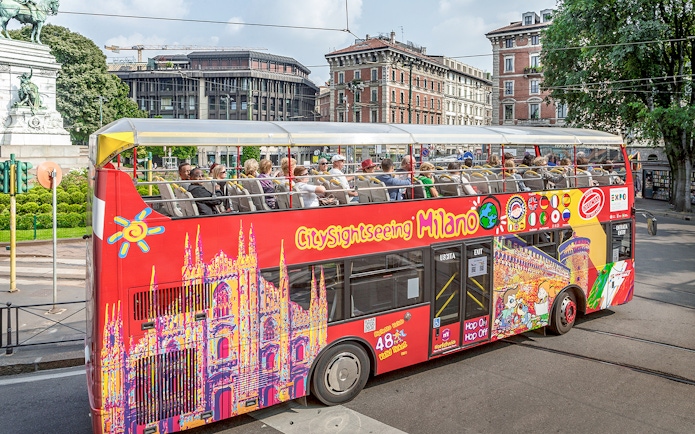 City Sightseeing Milan hop-on hop-off bus with tourists near historical buildings.