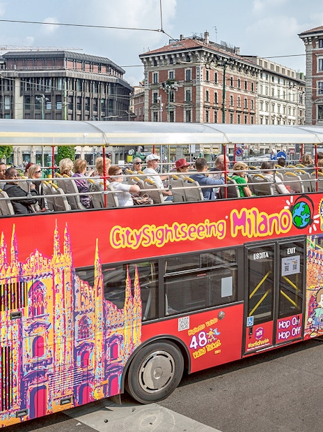 City Sightseeing Milan hop-on hop-off bus with tourists near historical buildings.