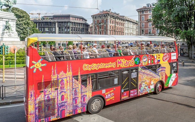 City Sightseeing Milan hop-on hop-off bus with tourists near historical buildings.
