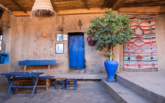 Berber house interior with blue door, woven rug, and wooden furniture in Ourika Valley, Morocco.