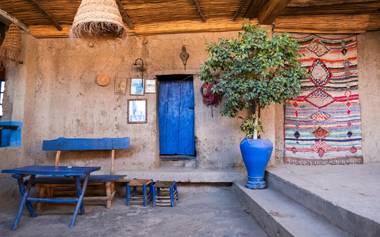 Berber house interior with blue door, woven rug, and wooden furniture in Ourika Valley, Morocco.