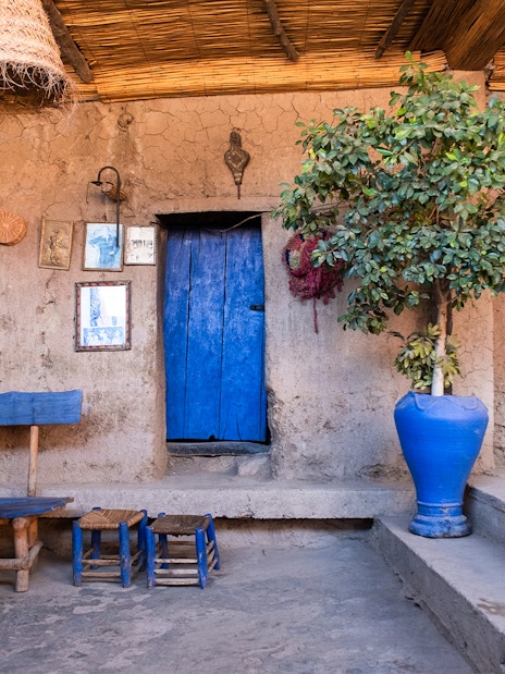 Berber house interior with blue door, woven rug, and wooden furniture in Ourika Valley, Morocco.