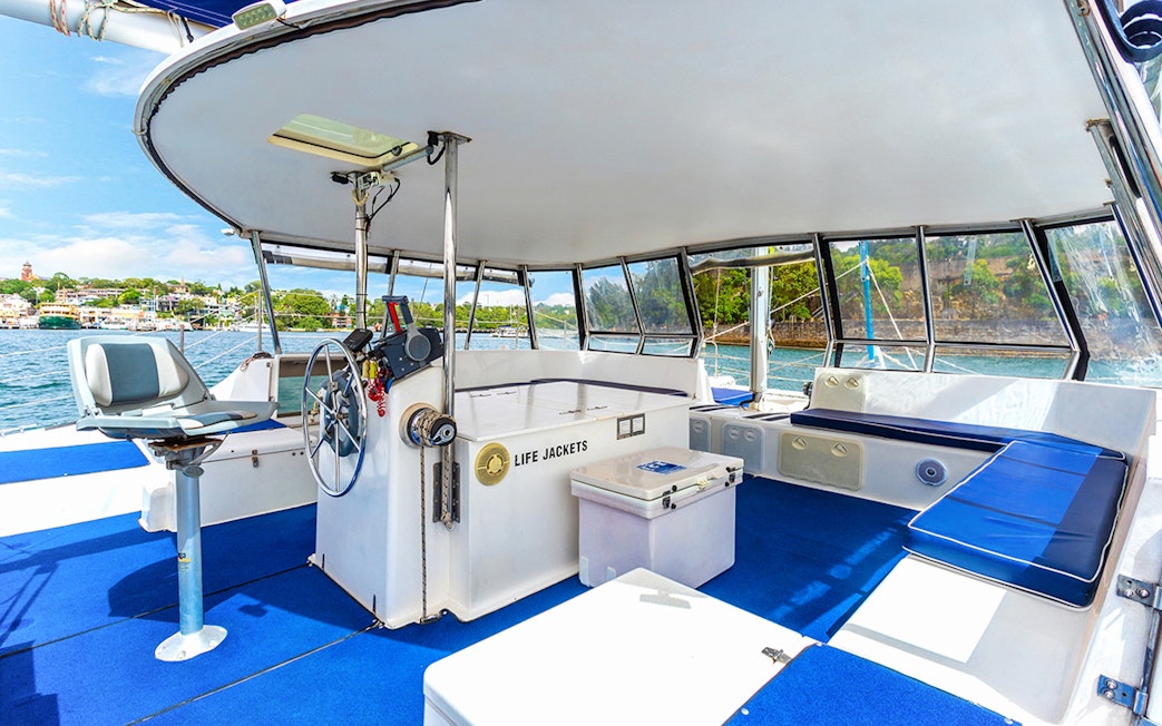 Catamaran interior with seating and steering wheel on Vivid Sydney BYO Kirralee Cruise.
