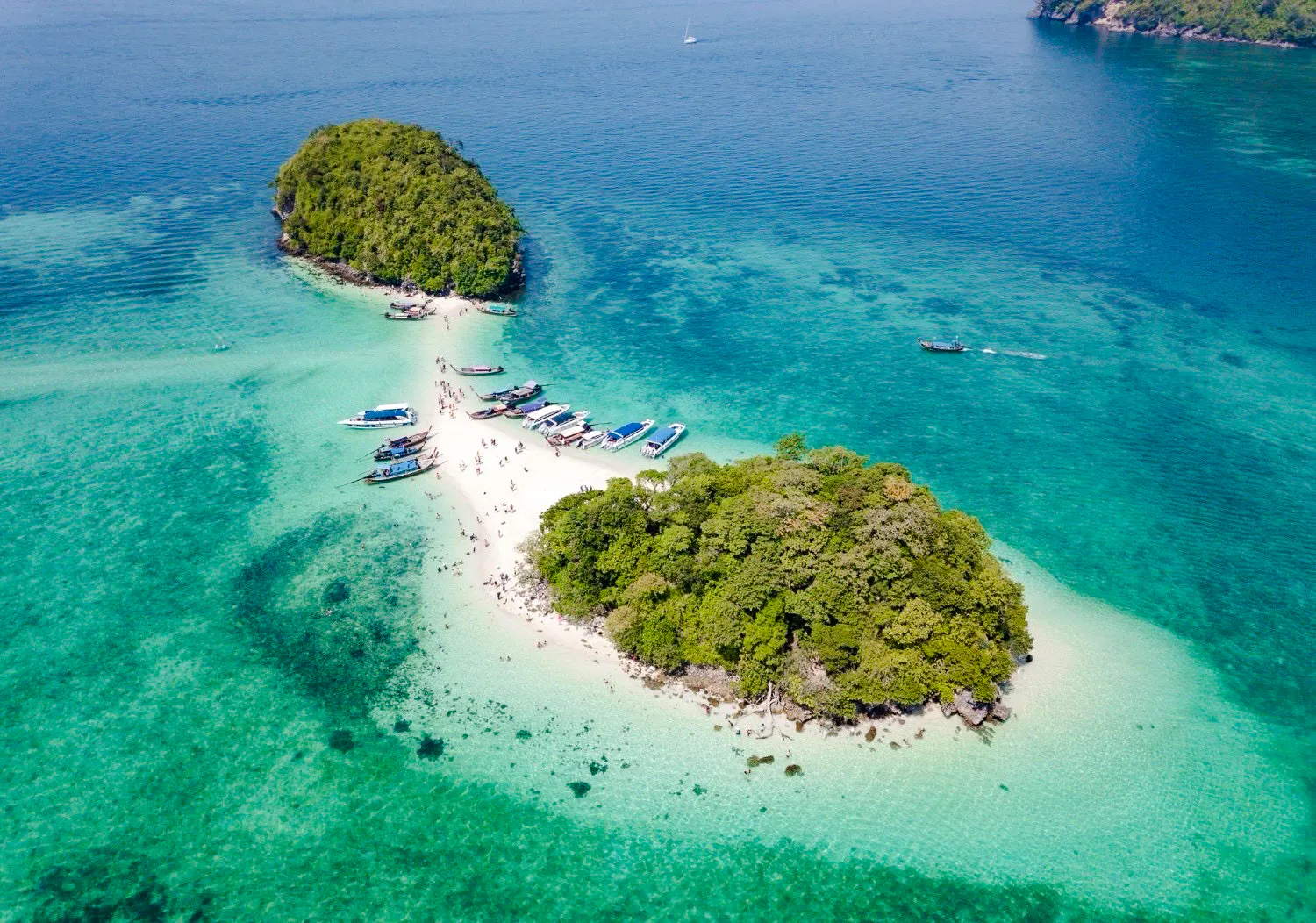 Aerial view of Krabi's 4 Islands with longtail boats and tourists on sandy beach.