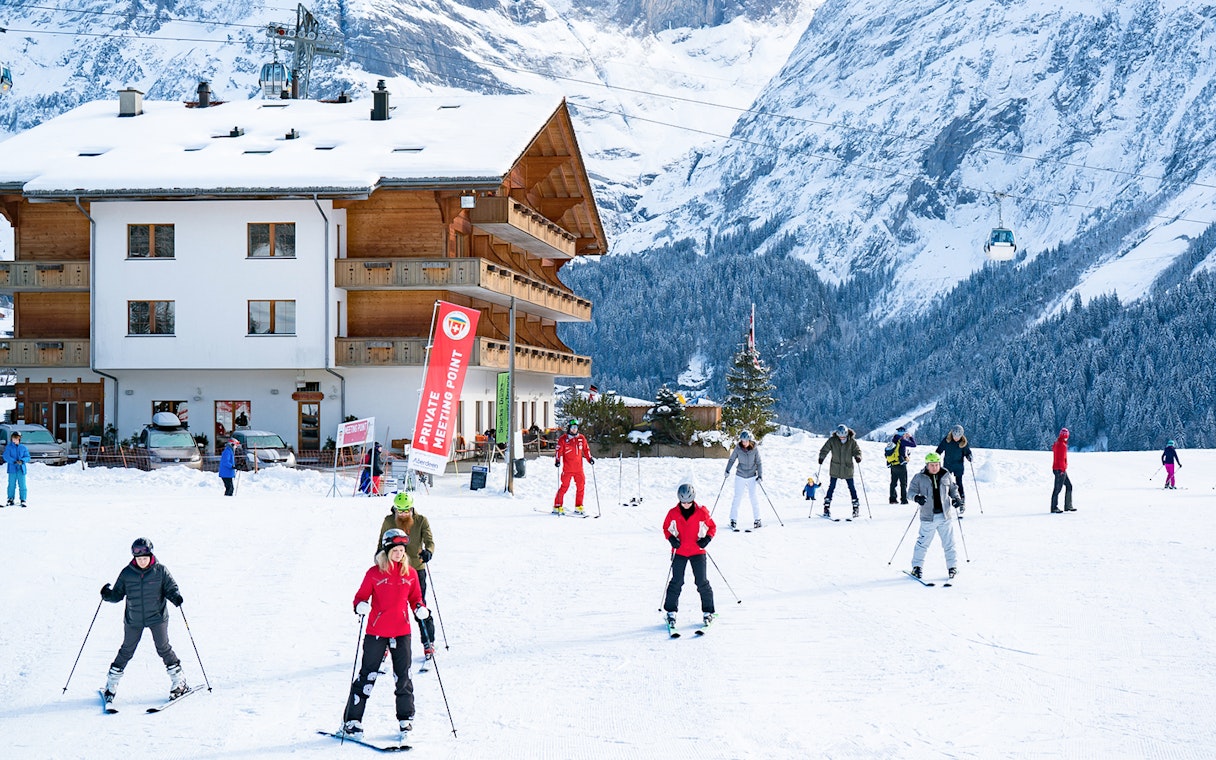 Beginner skiers practicing near a chalet in Grindelwald with snowy mountains in the background.