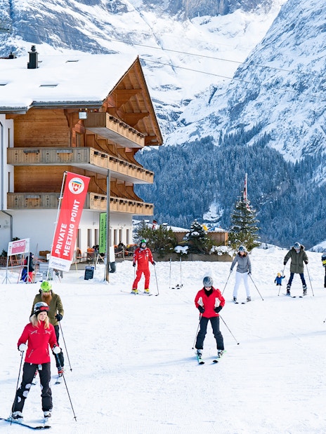 Beginner skiers practicing near a chalet in Grindelwald with snowy mountains in the background.