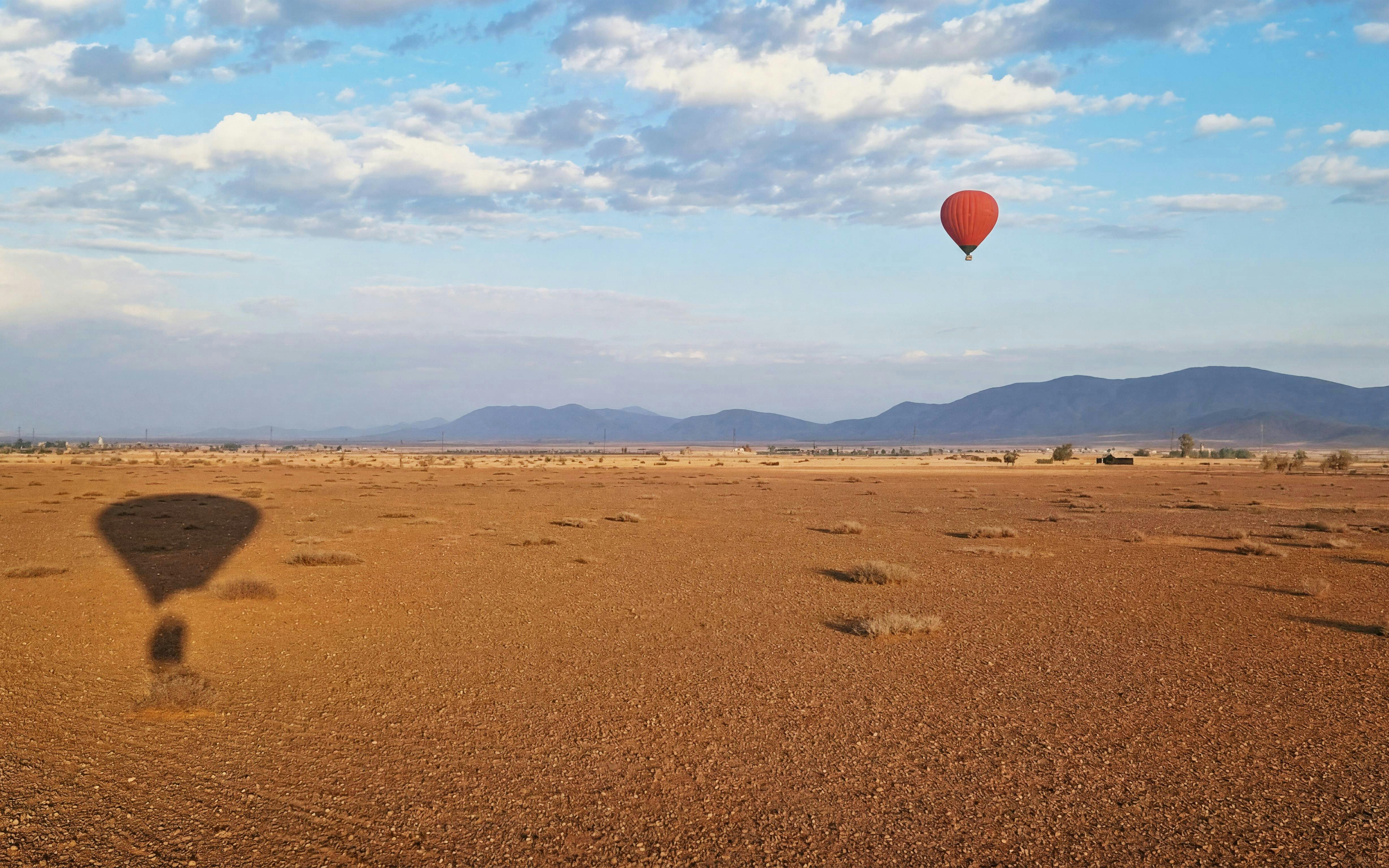 Hot air balloon over Marrakesh desert landscape at sunrise.