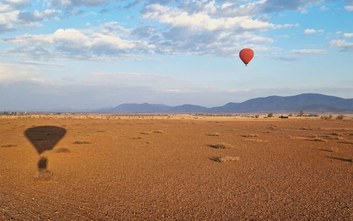 Hot air balloon over Marrakesh desert landscape at sunrise.