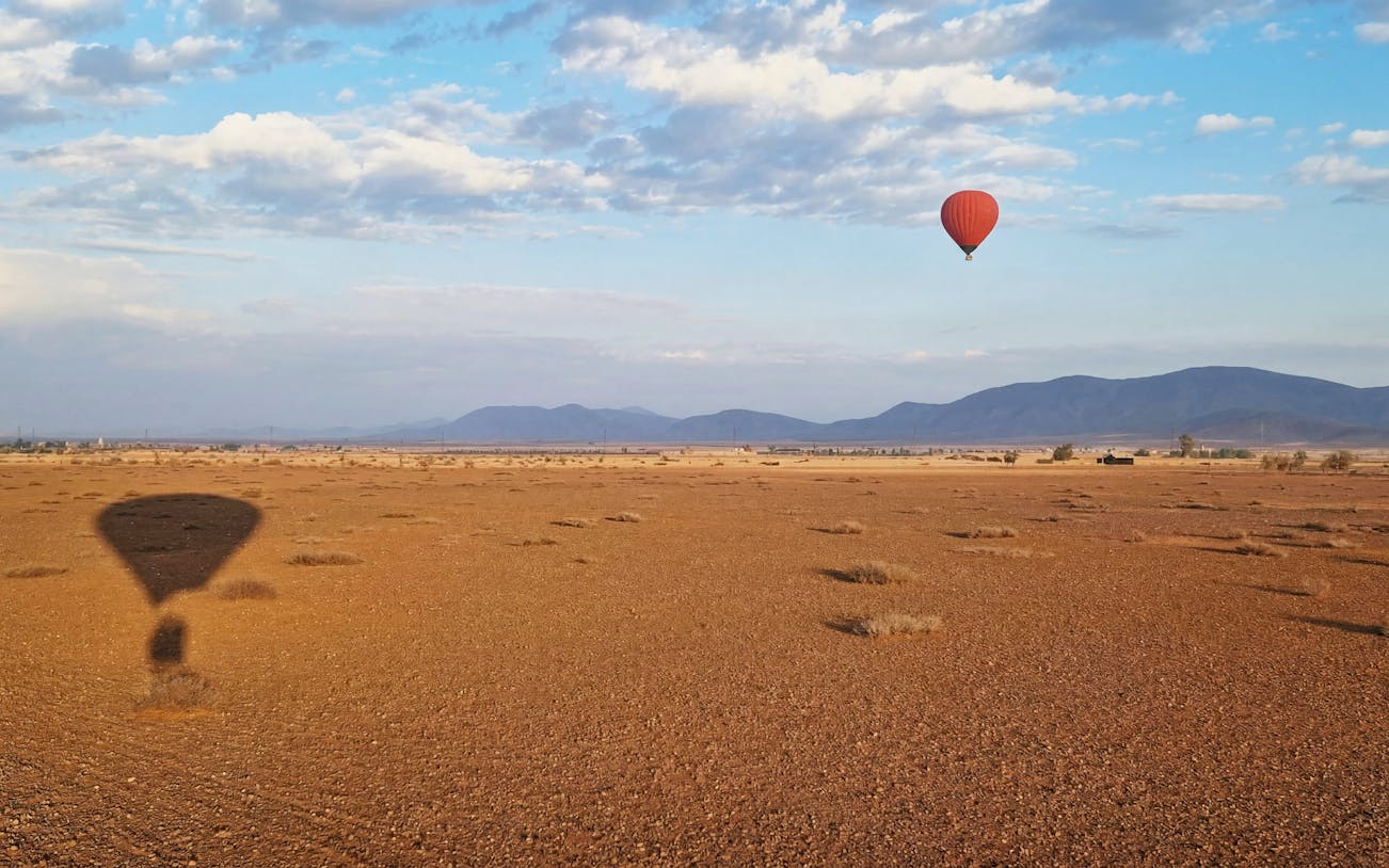 Hot air balloon over Marrakesh desert landscape at sunrise.