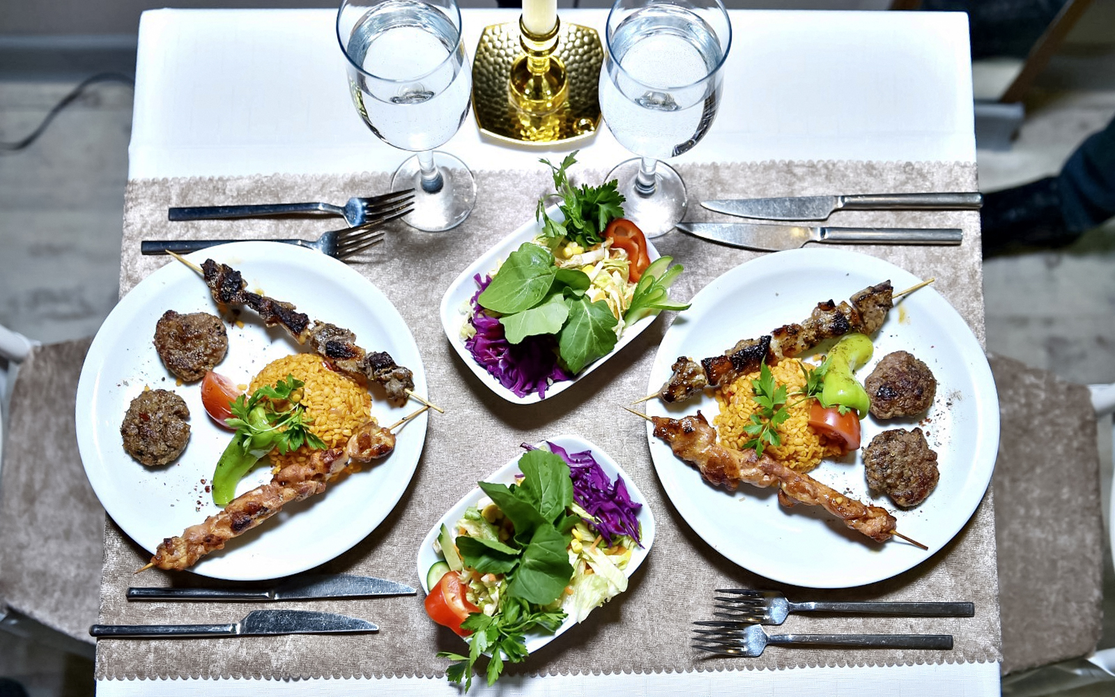 Plates of skewered meat, rice, and salad on a dinner table setting.