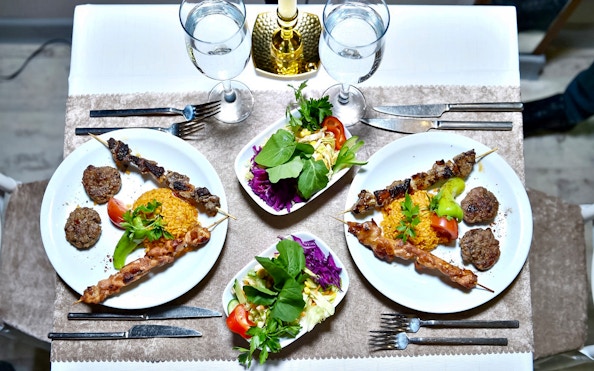 Plates of skewered meat, rice, and salad on a dinner table setting.