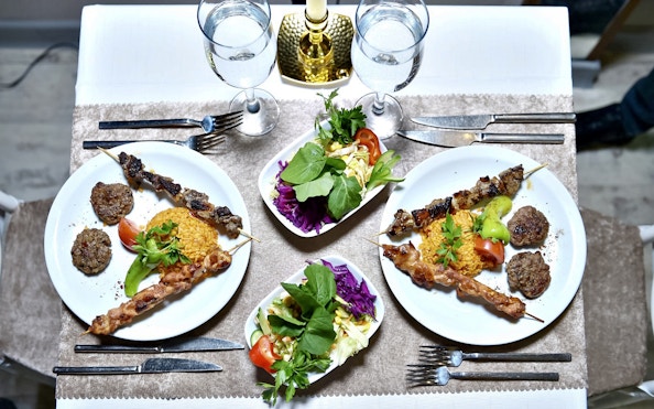 Plates of skewered meat, rice, and salad on a dinner table setting.