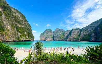 Tourists enjoying the beach at Maya Bay, Krabi, with limestone cliffs in the background.