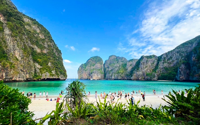 Tourists enjoying the beach at Maya Bay, Krabi, with limestone cliffs in the background.