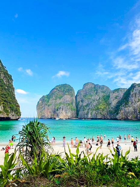 Tourists enjoying the beach at Maya Bay, Krabi, with limestone cliffs in the background.
