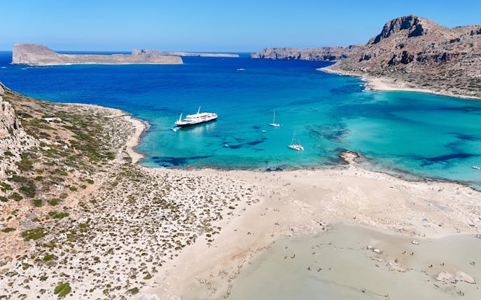 Boat cruise approaching Balos Lagoon, Crete, with turquoise waters and sandy beach.