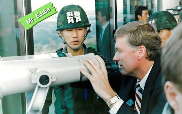 Man observing through binoculars with soldier nearby on DMZ Tour.