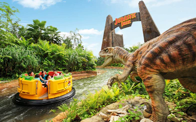 Visitors on Jurassic Park Rapids Adventure ride at Universal Studios Singapore, with dinosaur and jungle scenery.
