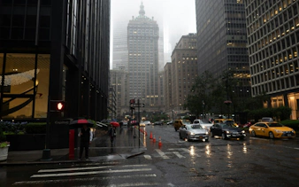 Rainy New York street with taxis and pedestrians, featuring historic skyscrapers.