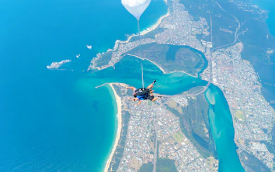 Skydiver tandem freefall over Newcastle Beach, Sydney, with coastal view.