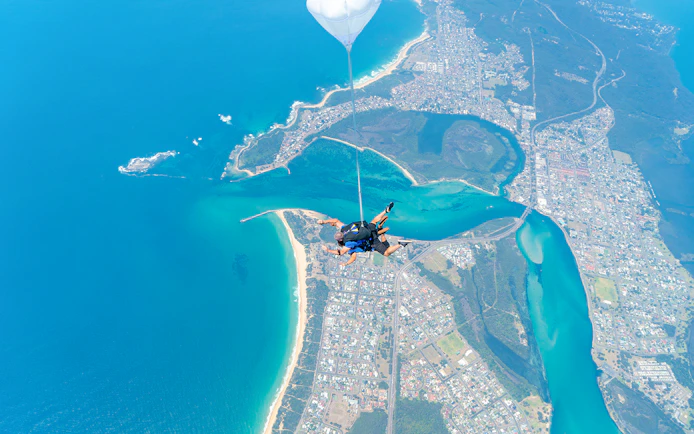 Skydiver tandem freefall over Newcastle Beach, Sydney, with coastal view.