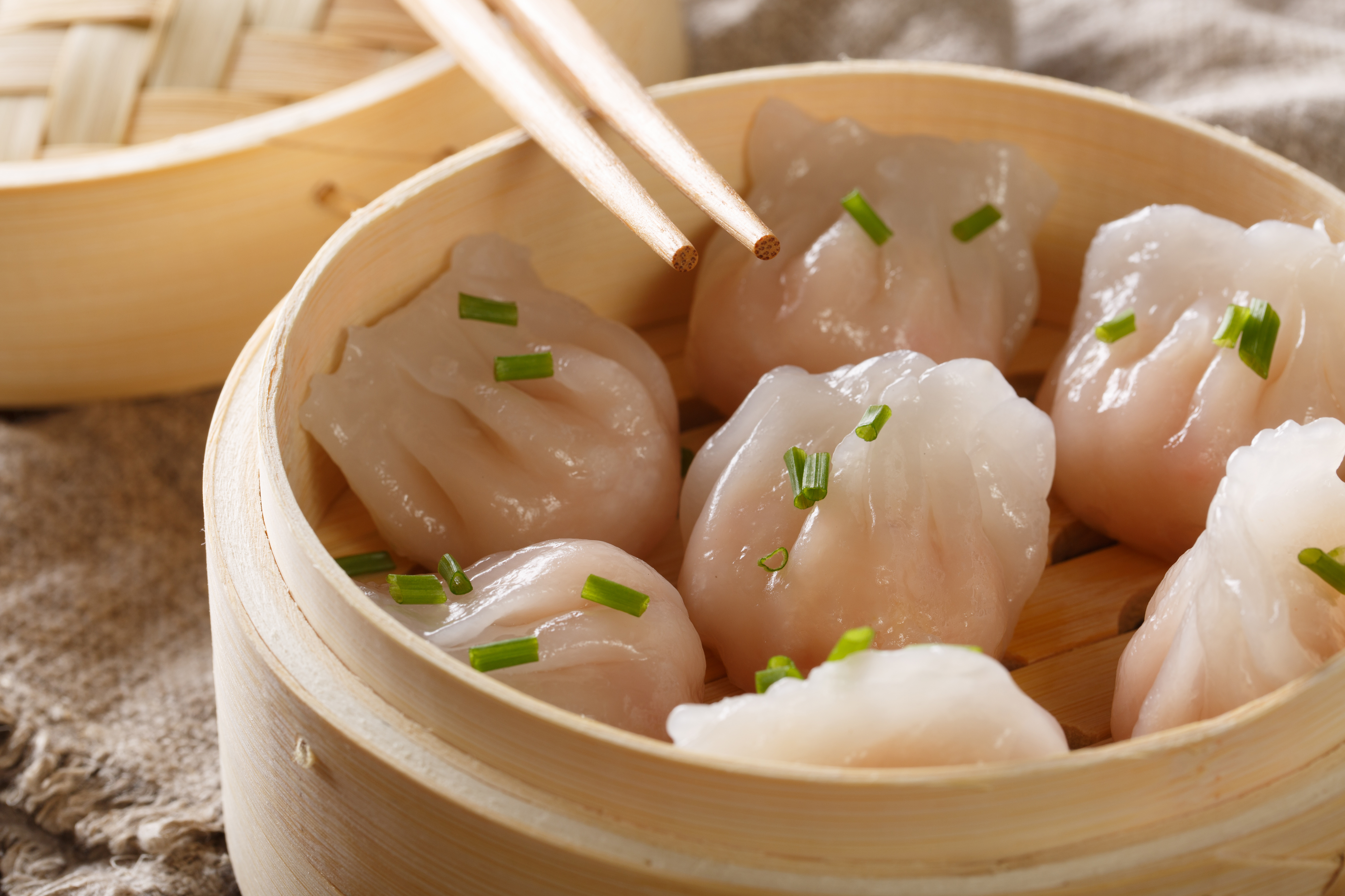 Steamed Chinese dumplings in bamboo basket with chopsticks.