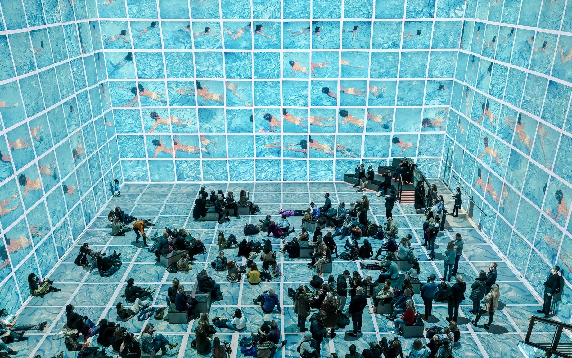Visitors viewing immersive David Hockney exhibition, "Bigger & Closer," with swimming pool visuals.