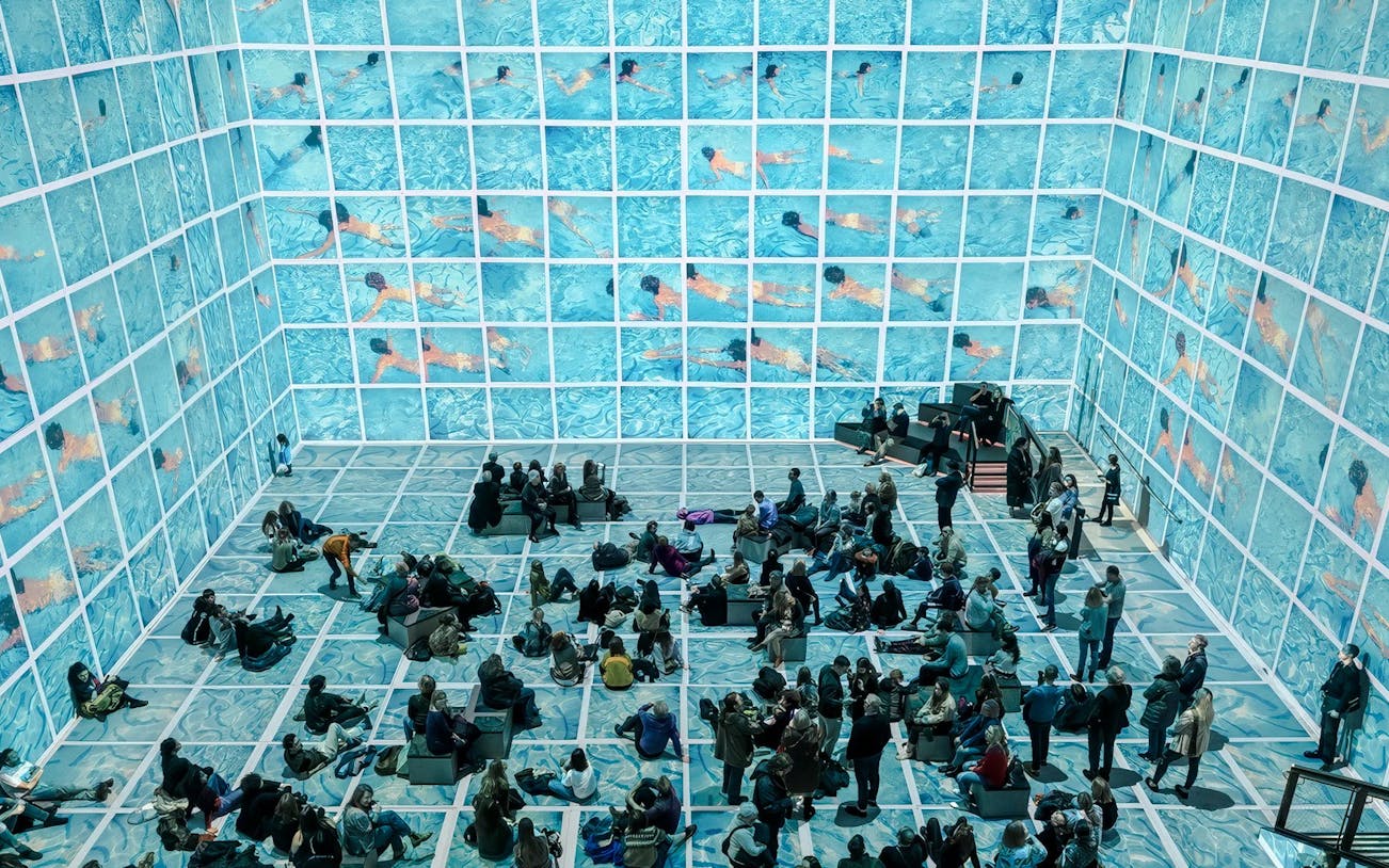 Visitors viewing immersive David Hockney exhibition, "Bigger & Closer," with swimming pool visuals.
