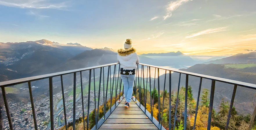 Person standing on Harder Kulm viewpoint platform overlooking sunset and mountains in Switzerland.