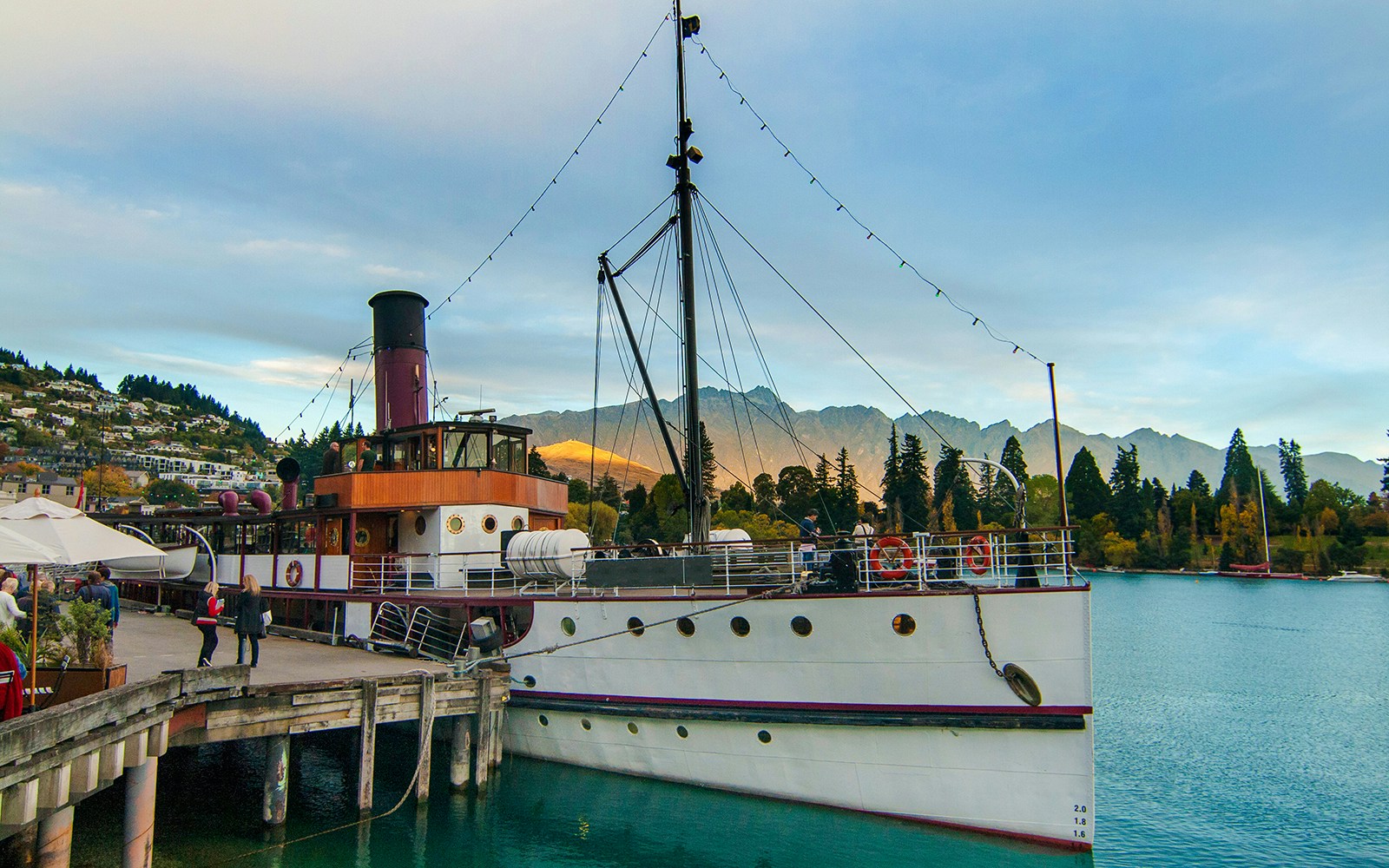 Historic steamship at Queenstown wharf with mountains at sunset.