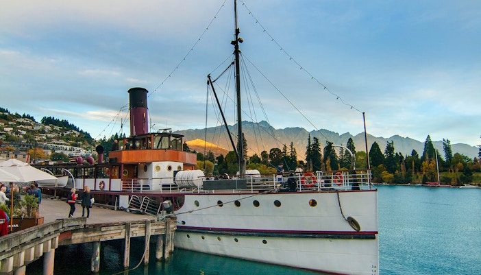 Historic steamship at Queenstown wharf with mountains at sunset.