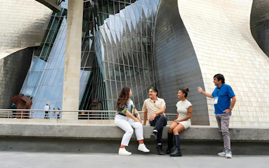Guggenheim Museum Bilbao exterior with visitors sitting and talking.