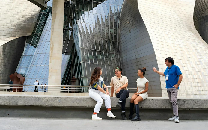 Guggenheim Museum Bilbao exterior with visitors sitting and talking.