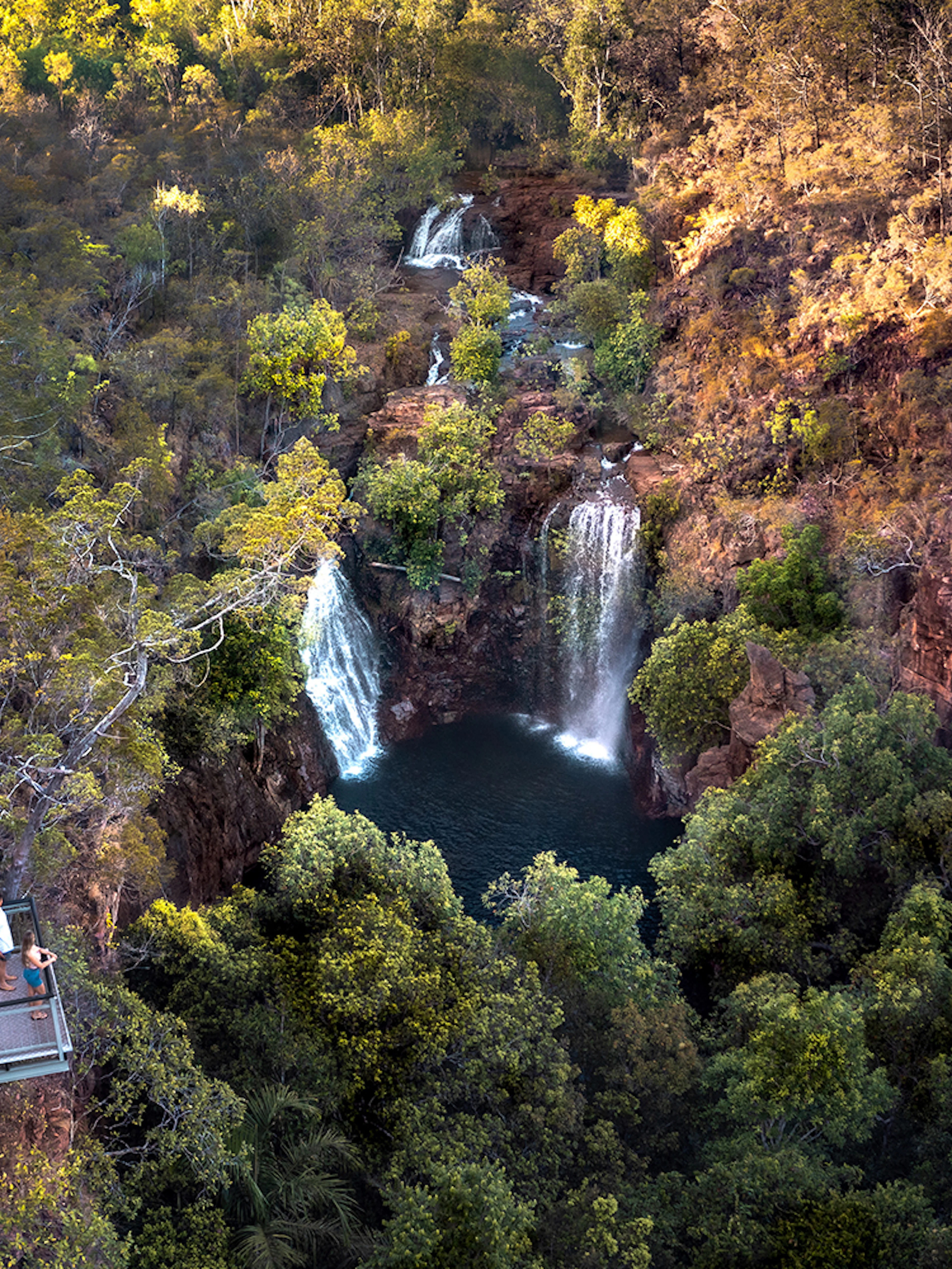 Litchfield National Park waterfall view from lookout platform, surrounded by lush greenery.
